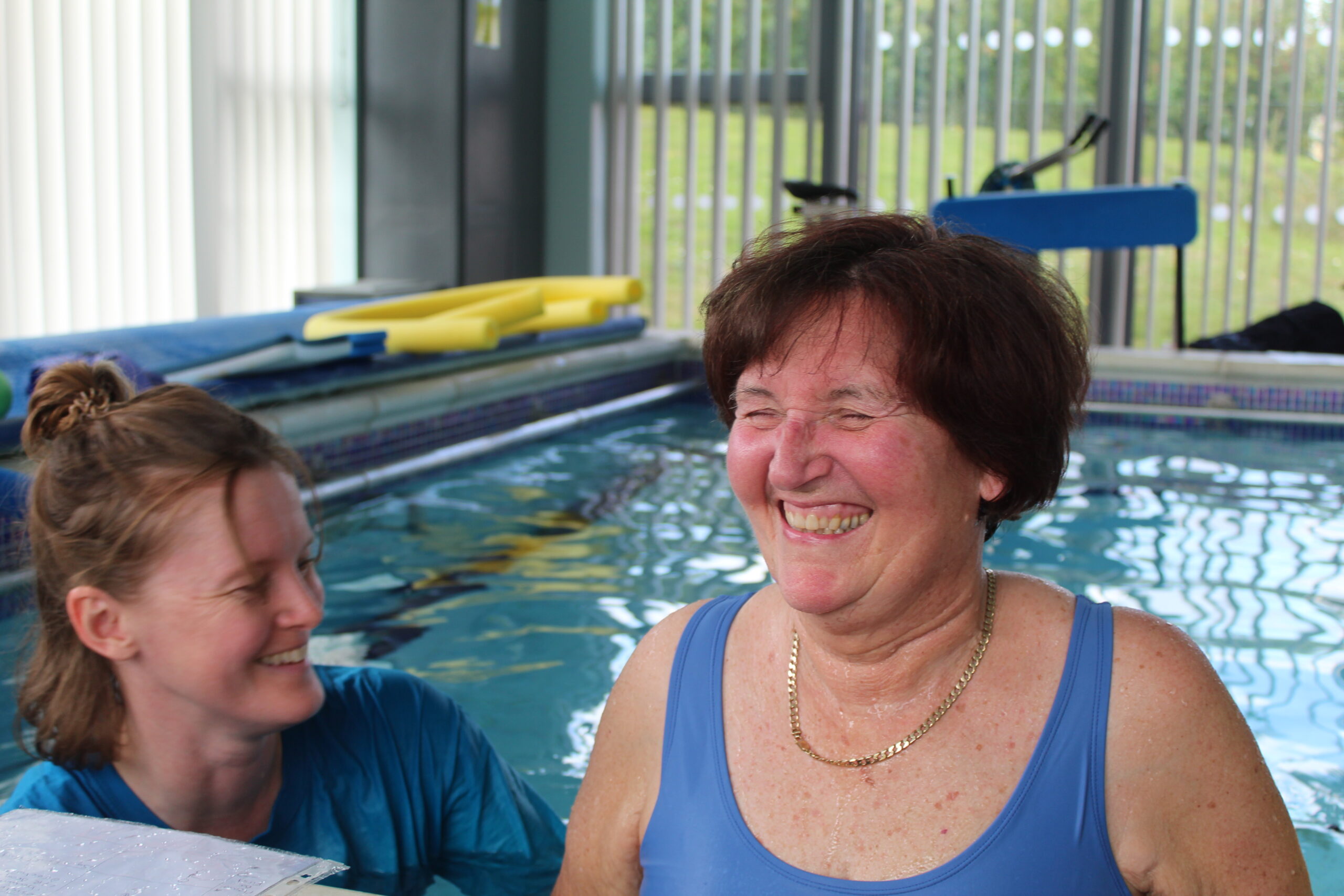 Lady smiling in the pool with a volunteer